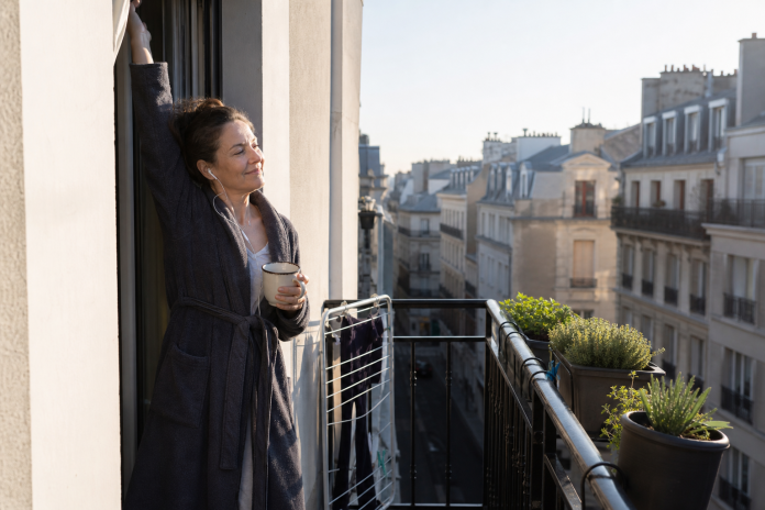 Woman on an apartment balcony in the morning with a mug, stretching in the sunlight