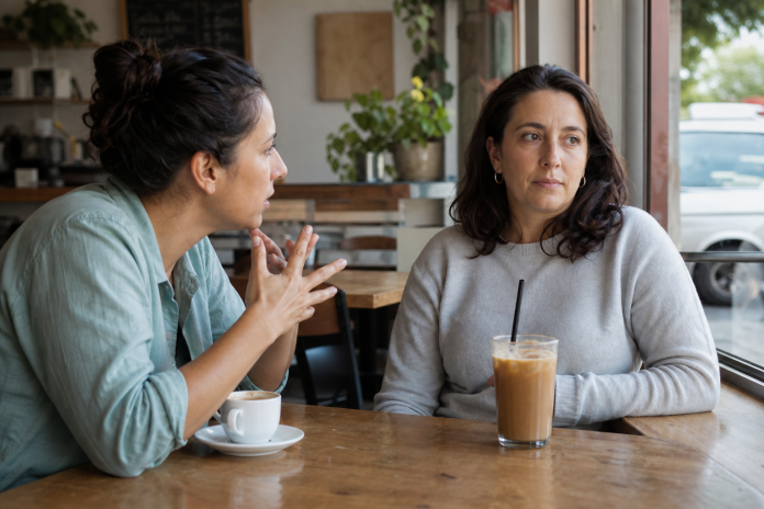 A draining conversation in a café Two women at a café window table, one talking intensely while the other looks tired and glances toward the door