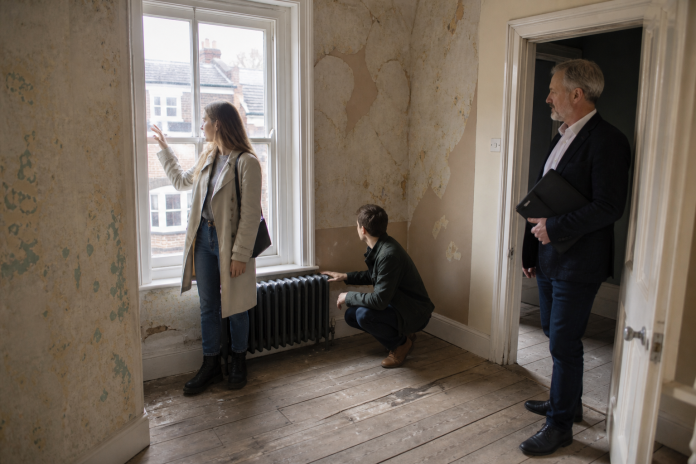 Checking an old house for draughts on a viewing Couple viewing an empty older house, one feeling for a draught at a sash window, the other checking an old radiator