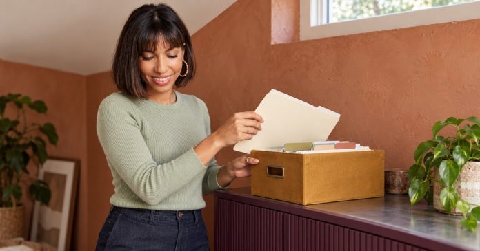 Woman placing a cream folder into an ochre file box on a plum cabinet