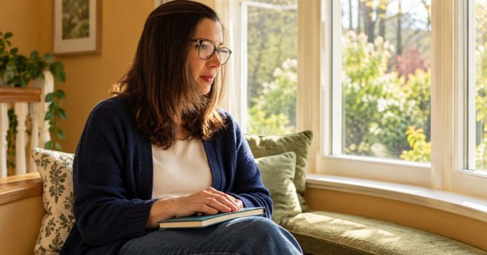 Negative Thoughts — A Balanced Reflective Pause Woman with green glasses resting her hands on a closed notebook beside a sunlit bay window.